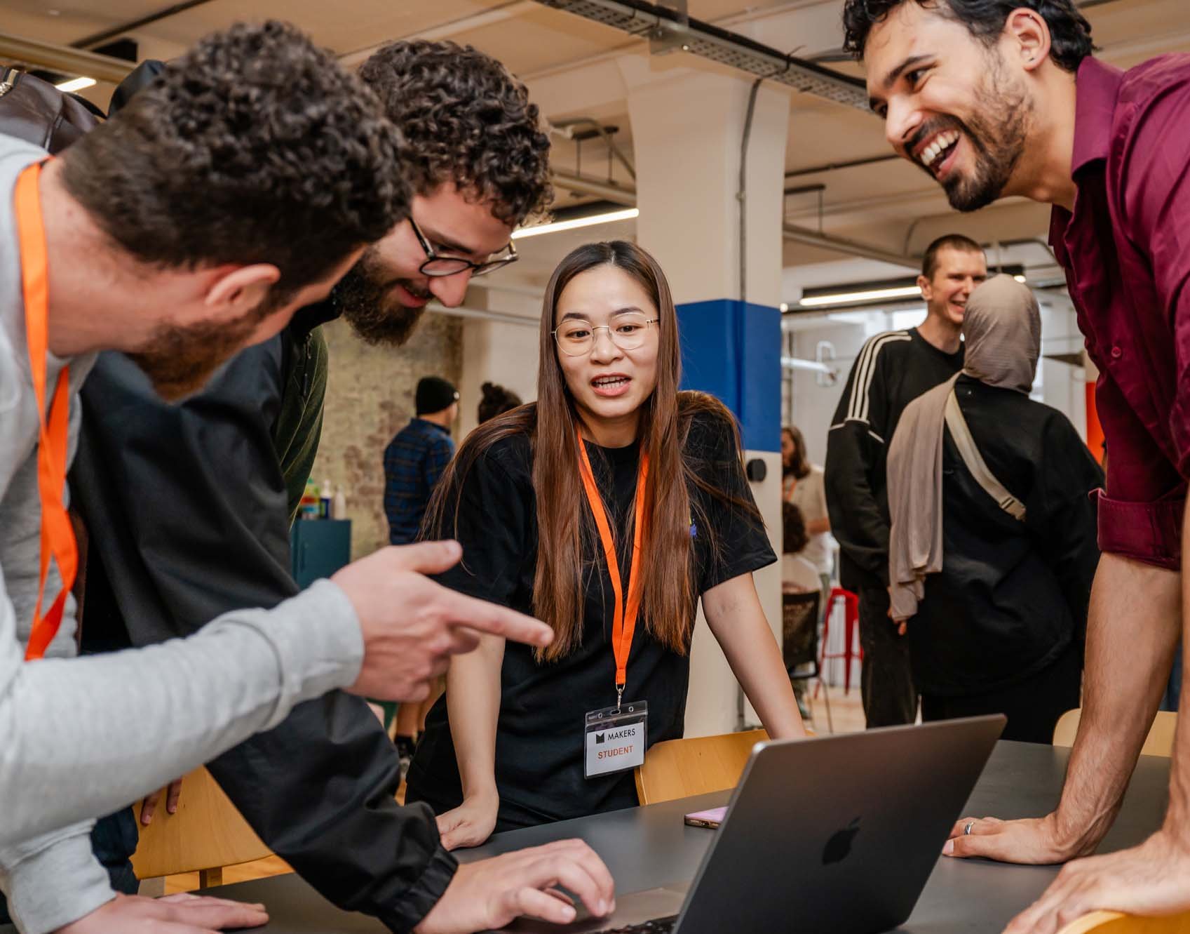 4 people debate energetically over a laptop while clusters of of people speak in the background