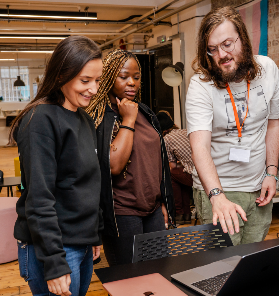 A male student explains his work to a female colleague and a female tutor. Someone works in the background of the large studio