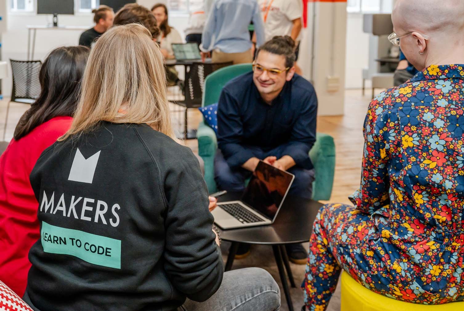 Students and talk together with a tutor around a laptop on a coffee table