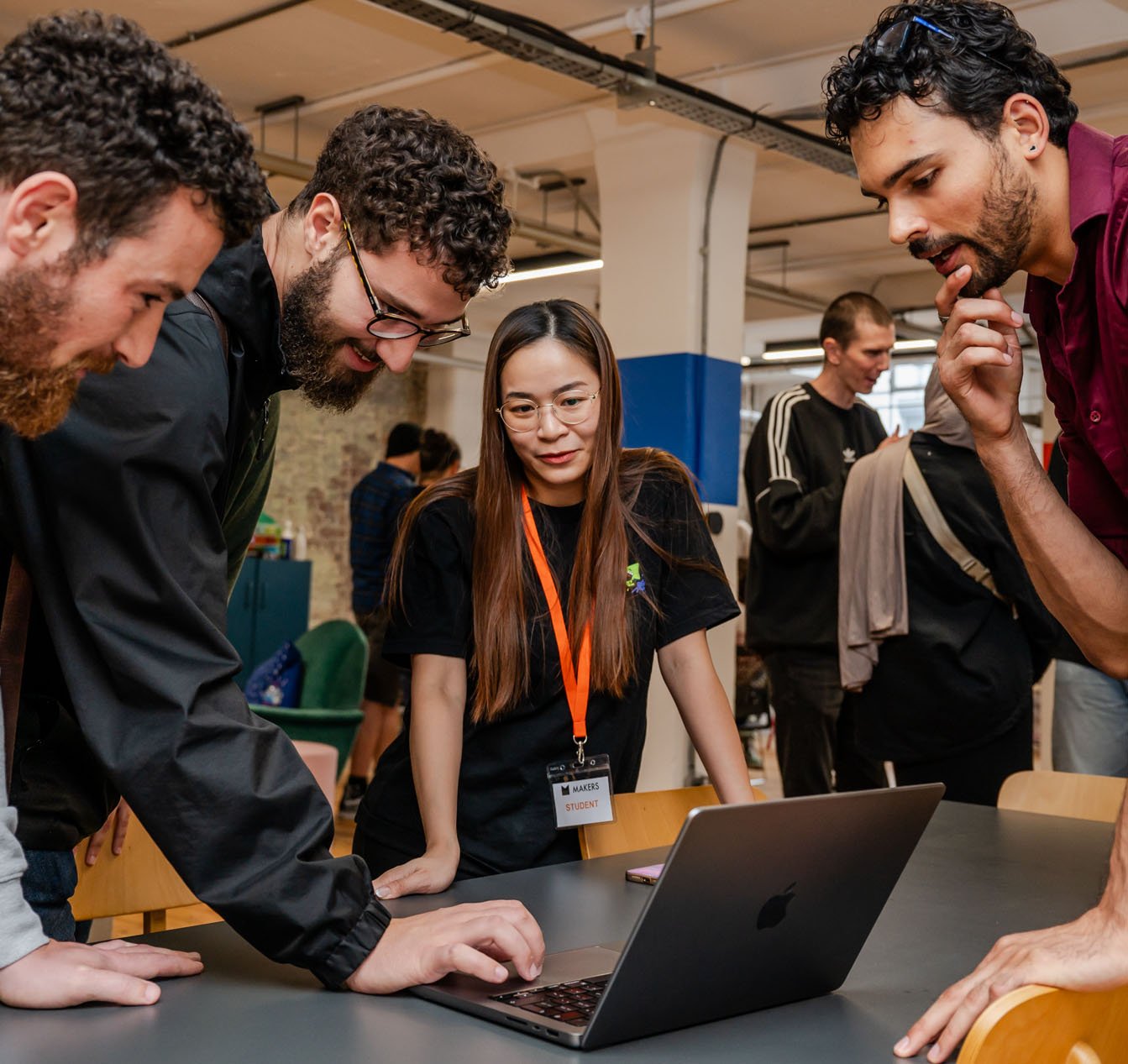3 men with dark curly hair and beards work on a laptop with female student with long hair and an orange langyard